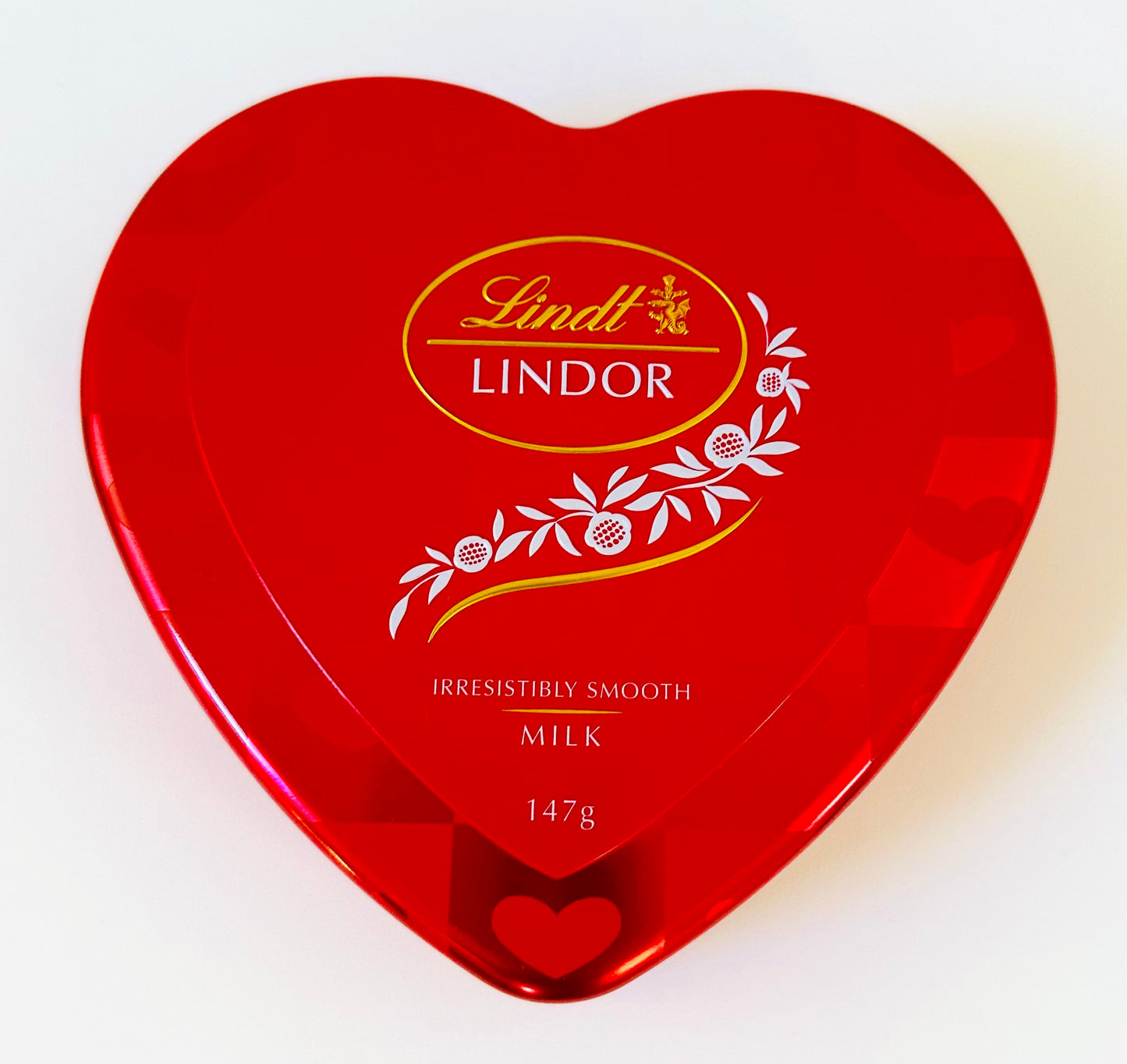 Red heart-shaped Lindt Lindor milk chocolate box, 147g, with floral design on lid.