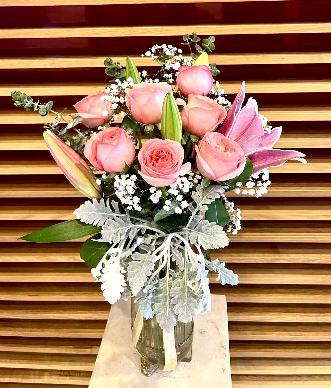 Pink rose and lily bouquet with greenery and baby's breath in a glass vase