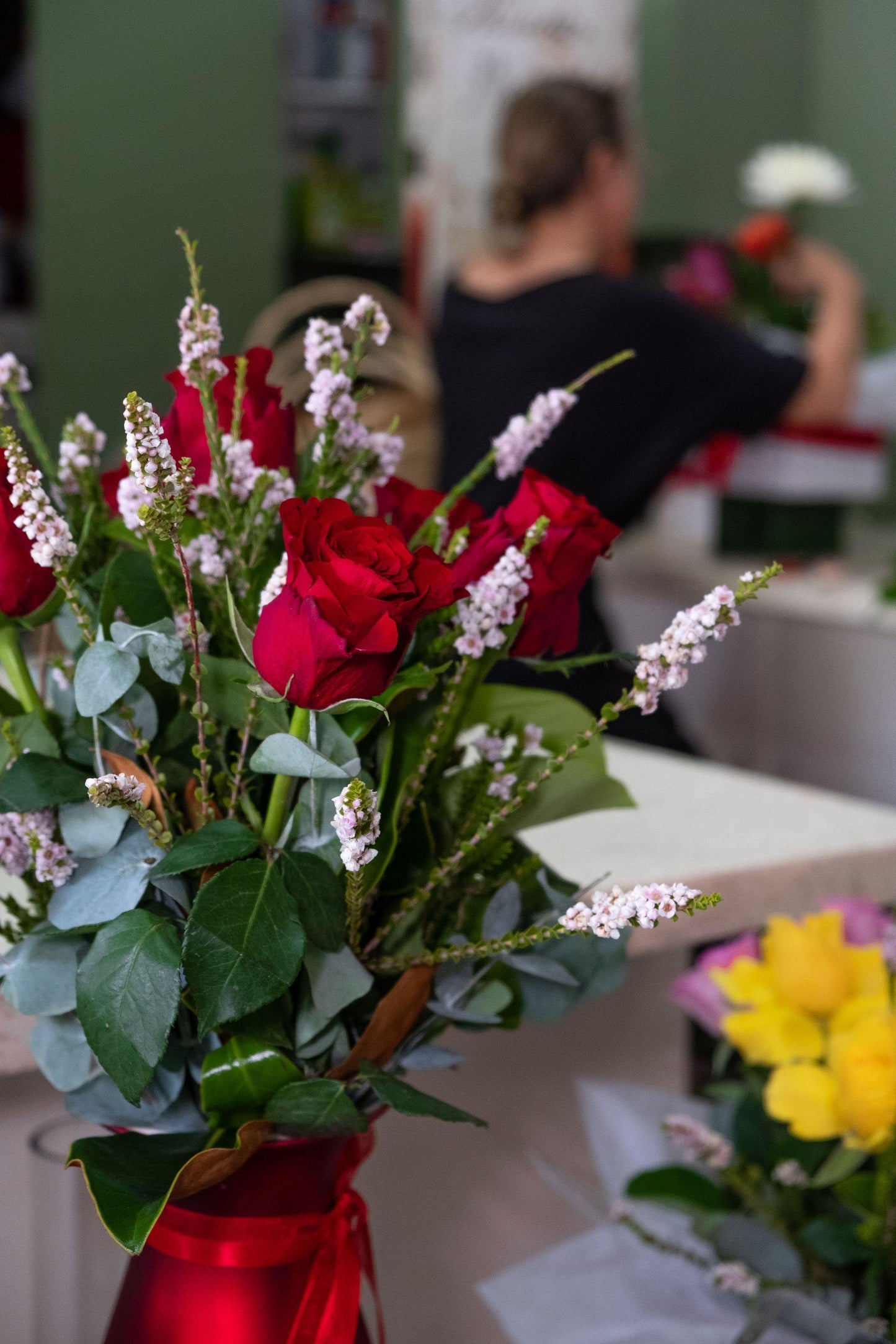 Fresh red rose bouquet with greenery and pink accents in a florist shop setting