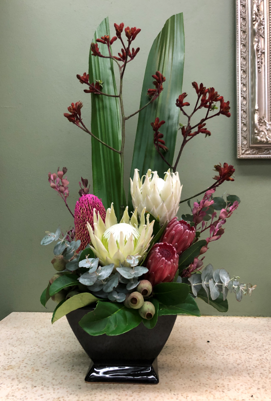 Native Australian flower arrangement with proteas, eucalyptus, and greenery in a black vase