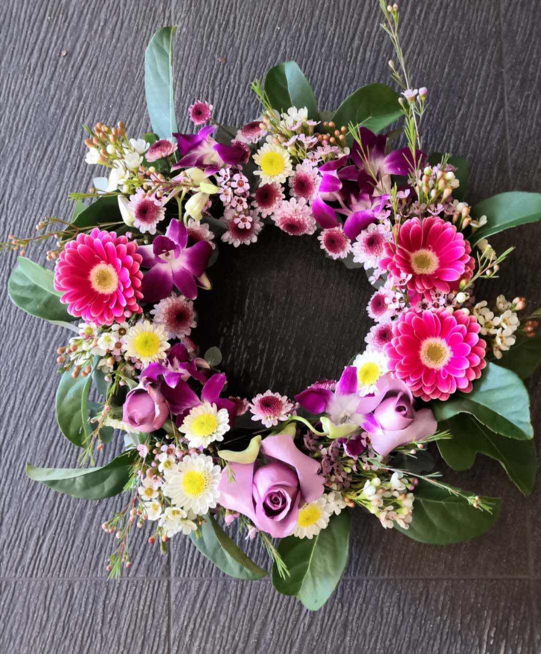 Fresh floral wreath with pink roses, orchids, daisies, and greenery on dark textured background