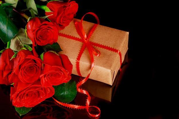 Bouquet of red roses with gift box tied with red ribbon on black background