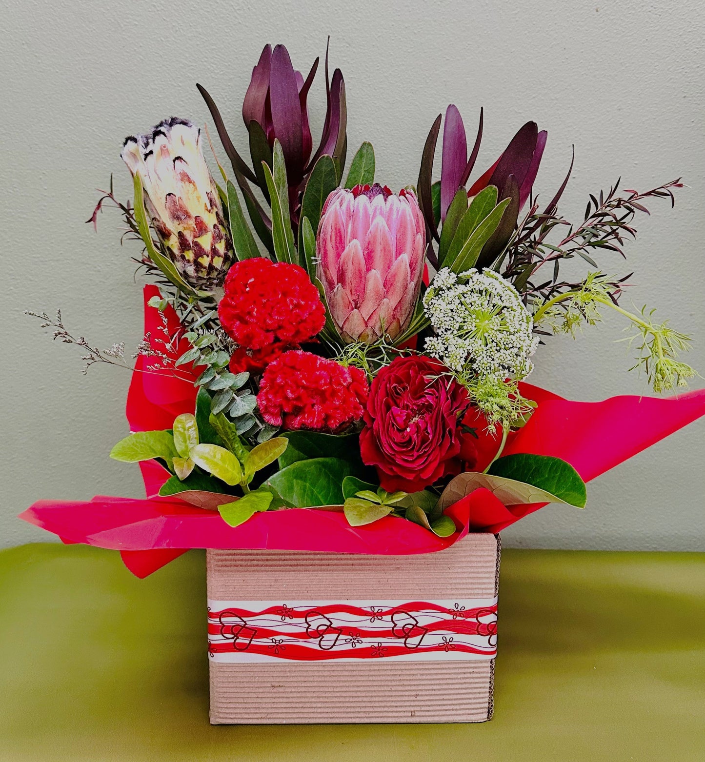 Vibrant native flower arrangement with protea, red roses, greenery in gift box with red wrap