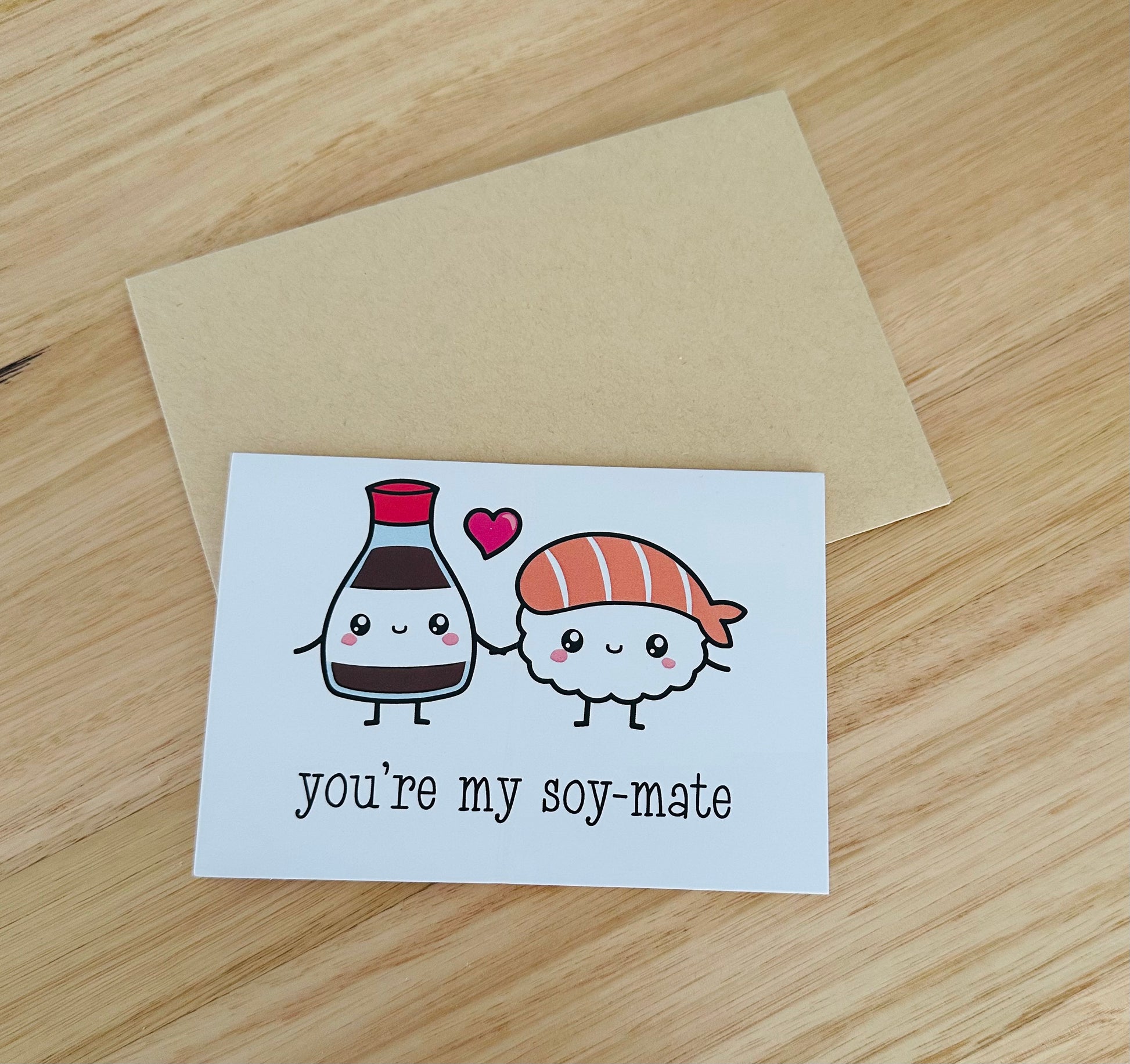 Cute greeting card with cartoon soy sauce and sushi, heart, and text you're my soy-mate on wood table