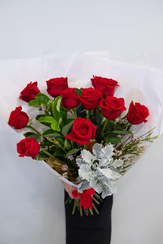 Bouquet of 12 fresh red roses with greenery and white paper wrap, ideal for flower delivery.