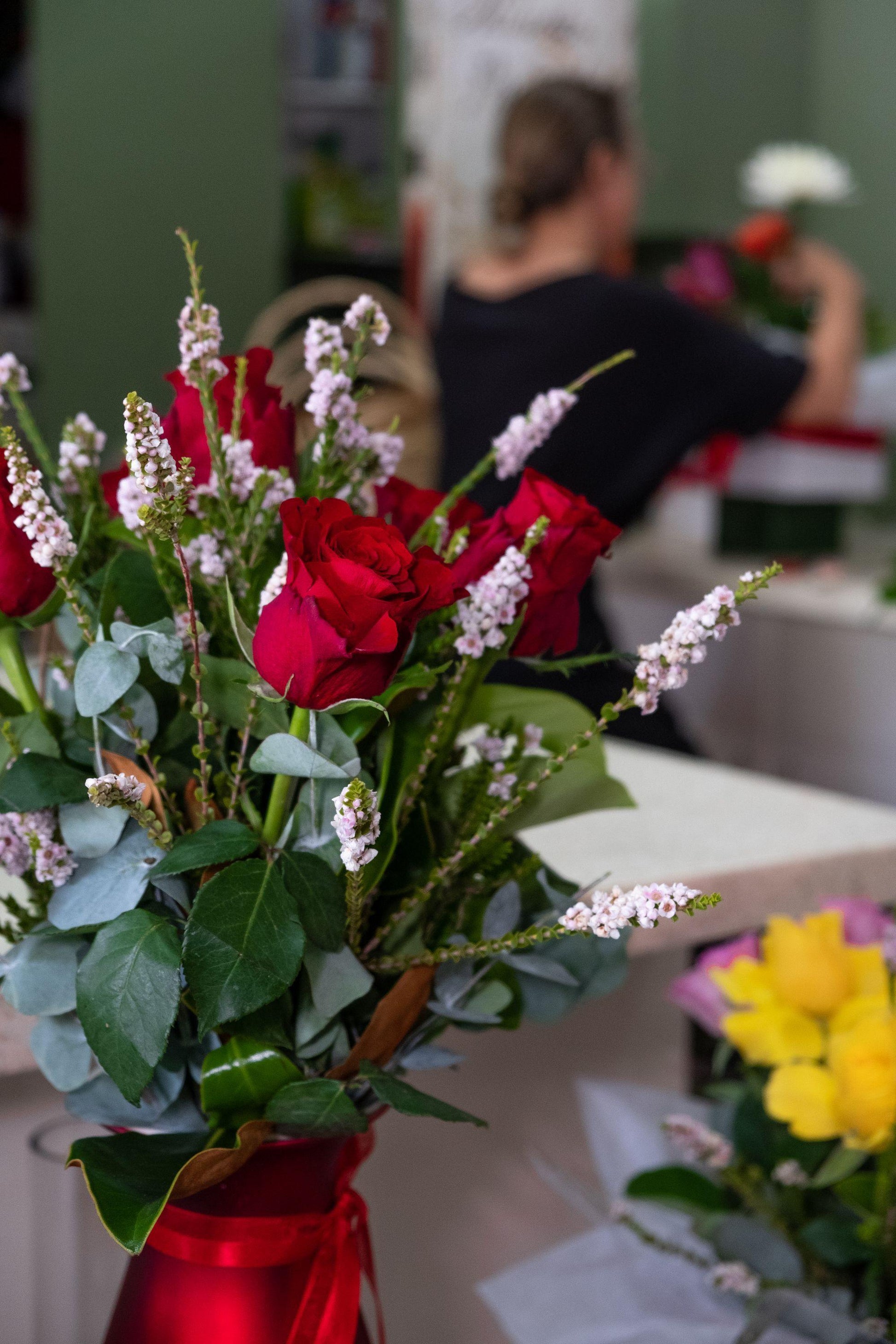 Fresh red rose bouquet with greenery and pink accents in a florist shop setting