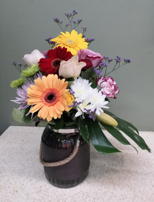 Mixed gerbera daisies, roses, chrysanthemums and carnations in a rustic jar vase arrangement