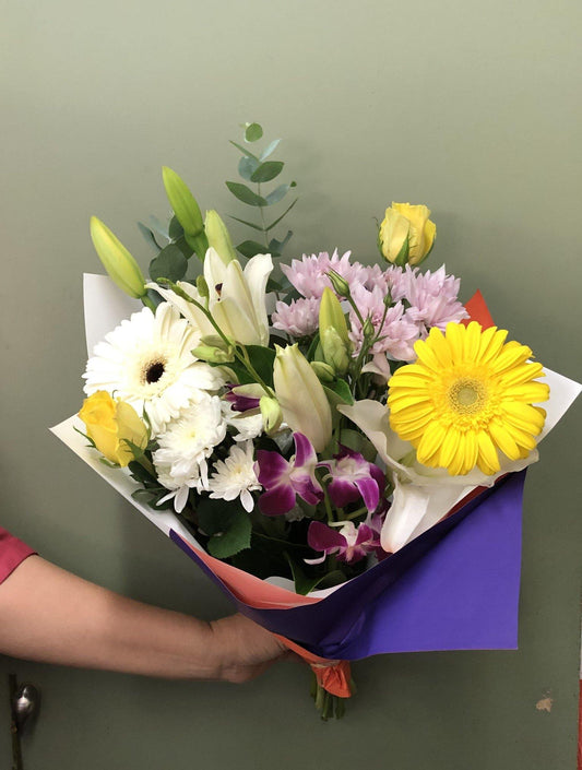 Mixed flower bouquet with yellow gerbera, white lilies, purple orchids, and yellow roses.