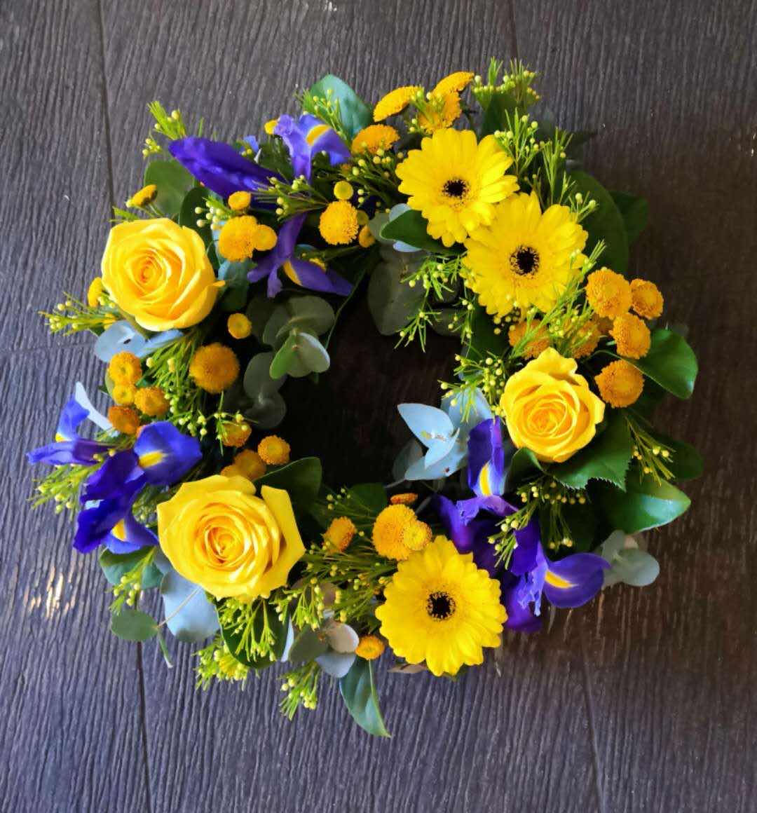 Vibrant floral wreath with yellow roses, gerberas, and purple irises on a dark background